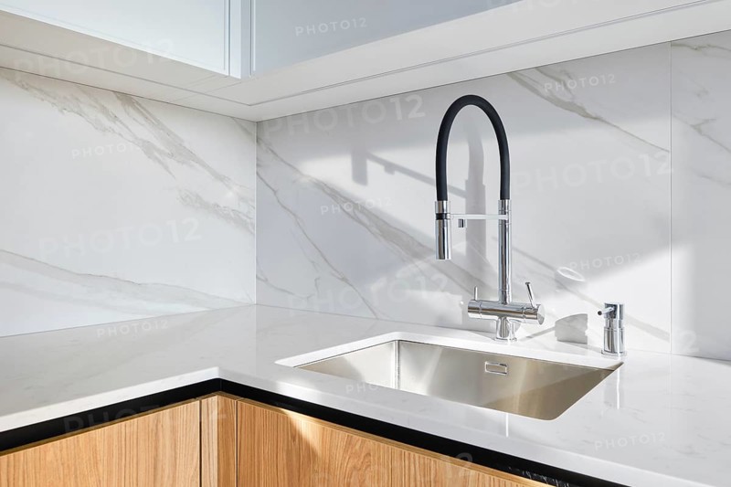 A contemporary kitchen showcases a stylish sink integrated into smooth marble countertop. The minimalist design includes elegant cabinetry and modern fixtures, offering a clean aesthetic