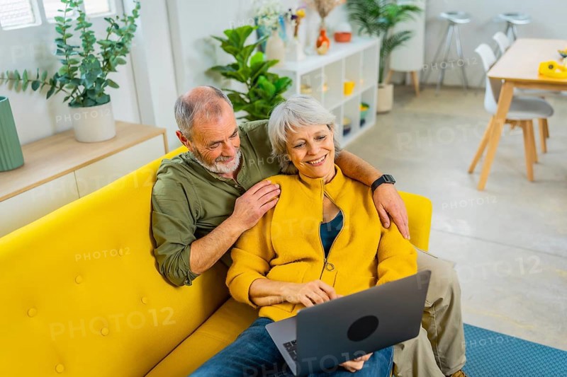 Elevated view photo of a casual senior couple lying on the sofa relaxed using laptop