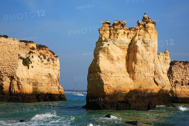 Praia do Pinhao, Lagos, Algarve, Portugal, Majestic coastal landscape with steep cliffs and a narrow passage to the calm sea, where a boat sails in the distance, Europe