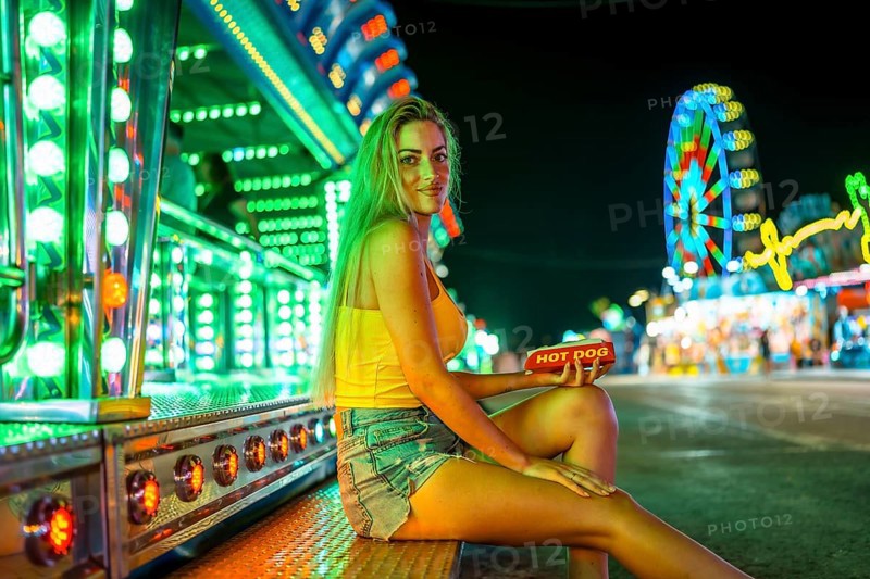 Blonde woman sitting alone about to eat a hot dog in a fair at night