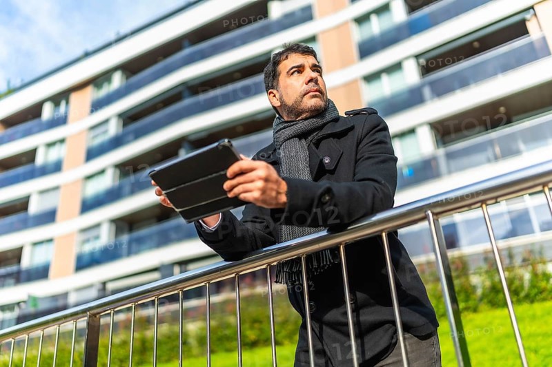 Low angle view portrait of a casual adult caucasian businessman using digital tablet leaning on rail at street