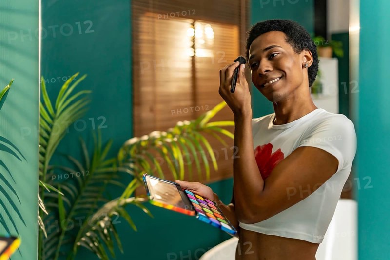 Reflection in the mirror of a happy gay man making up at home