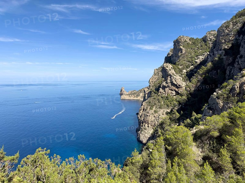 Rugged cliffs overlooking the deep blue sea, crossed by a boat on the water, Cala d'en Sardina, Ibiza, Balearic Islands, Spain, Europe