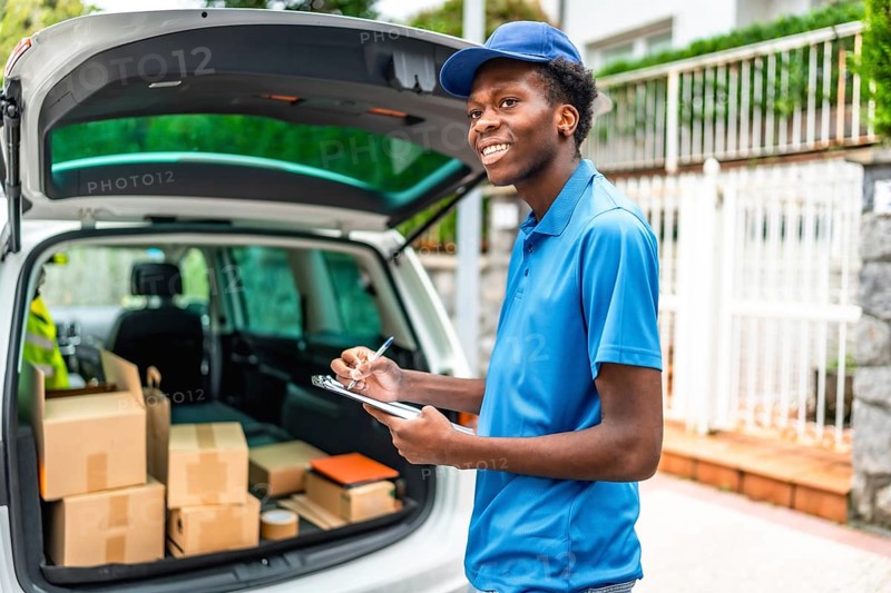 African delivery man in blue uniform verifying the packages on a van standing in the street