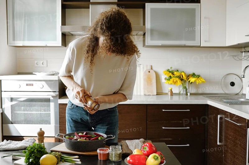 Woman sprinkles salt from manual spice mill on vegetables in a baking pan