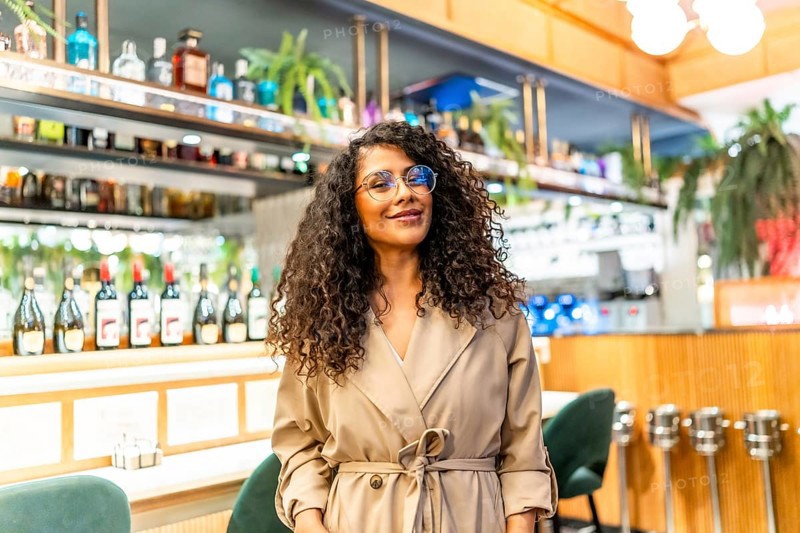 Beauty chic latin woman with curly hair and eyeglasses standing in a cafeteria smiling at camera