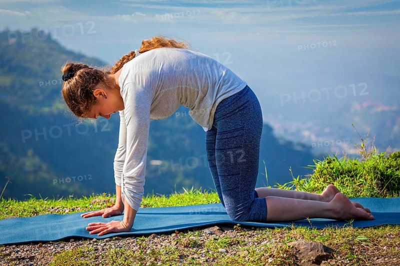 Yoga exercise outdoors, sporty fit woman practices yoga asana Marjariasana, cat pose outdoors in Himalayas