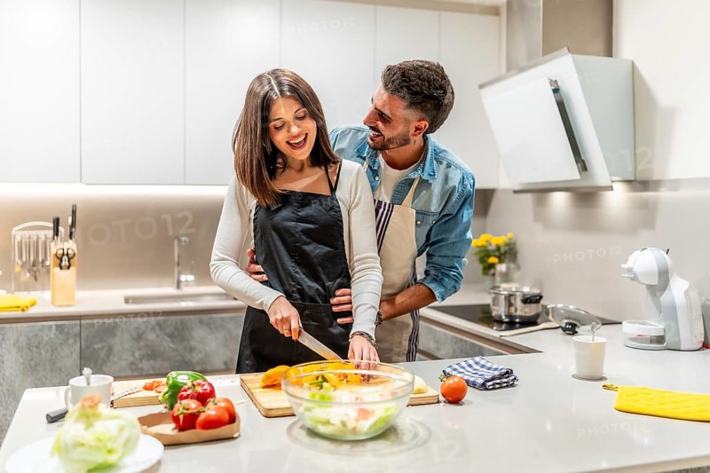 Young smiling couple wearing aprons preparing a healthy vegetable salad together in their modern kitchen