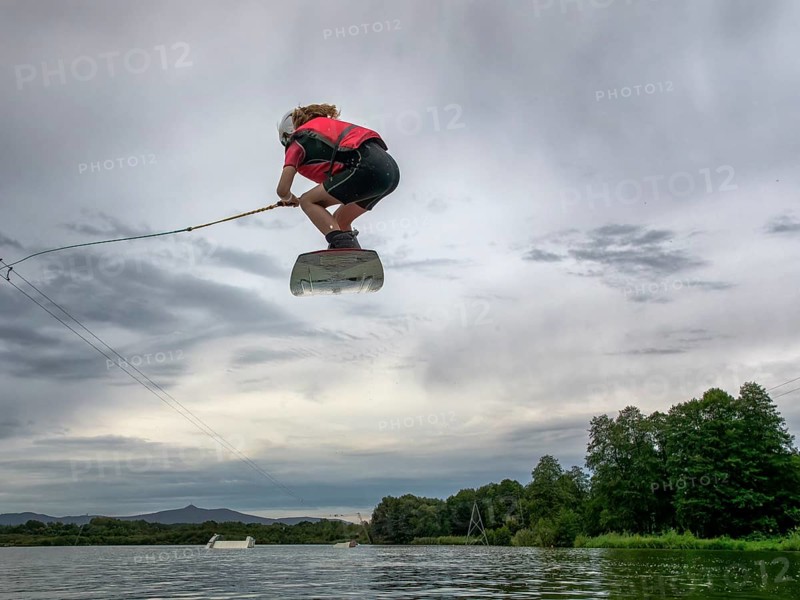 Boy or girl flies over the lake, jump with wakeboard, red life jacket, water skiing in wakepark, Stráž pod Ralskem, Czech Republic, Europe