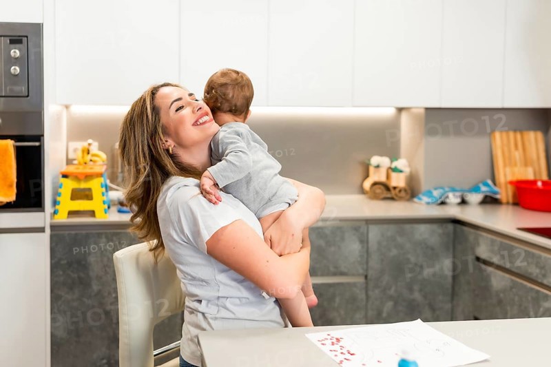 Mom lovingly embraces her baby in a modern kitchen, creating a heartwarming moment of family connection