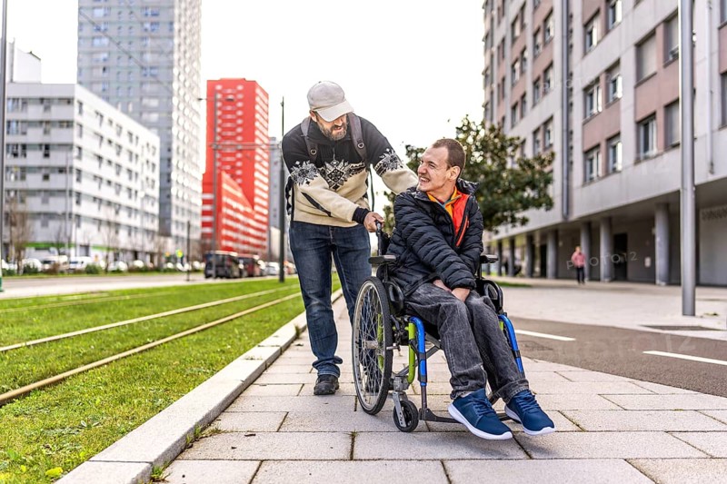 Caregiver assisting a young man with disability, strolling through a city environment, promoting inclusivity and support