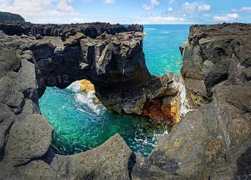Panoramic view of rugged lava rock formations with a natural arch over turquoise sea under blue sky, A Porta do Diabo, Sao Miguel Island, Azores, Portugal, Europe