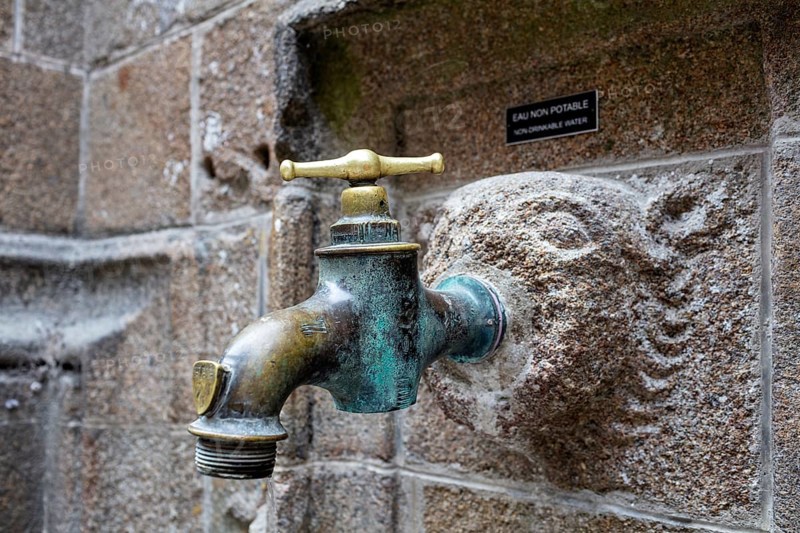 Old metal water tap on a weathered stone wall, Le Mont-Saint-Michel