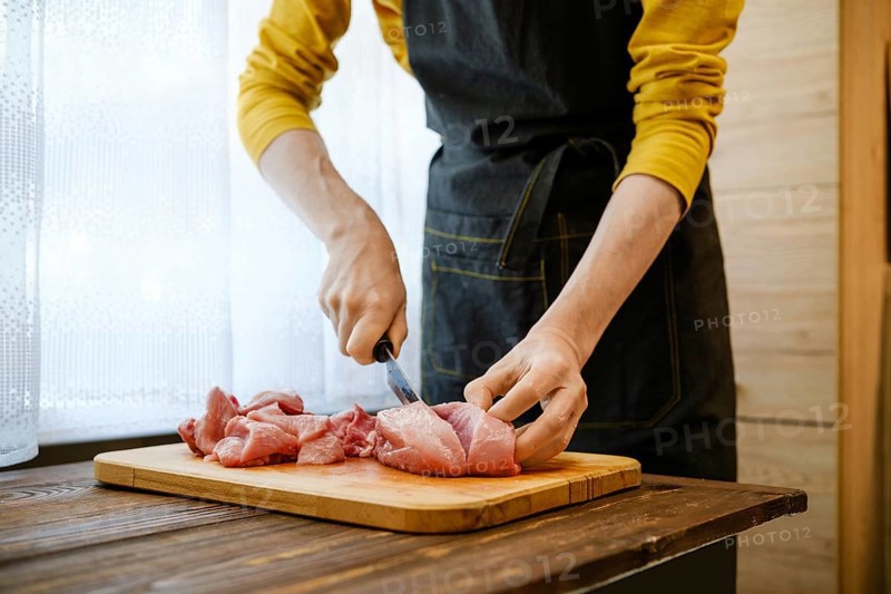 Unrecognizable man cuts pork meat into large pieces in the kitchen