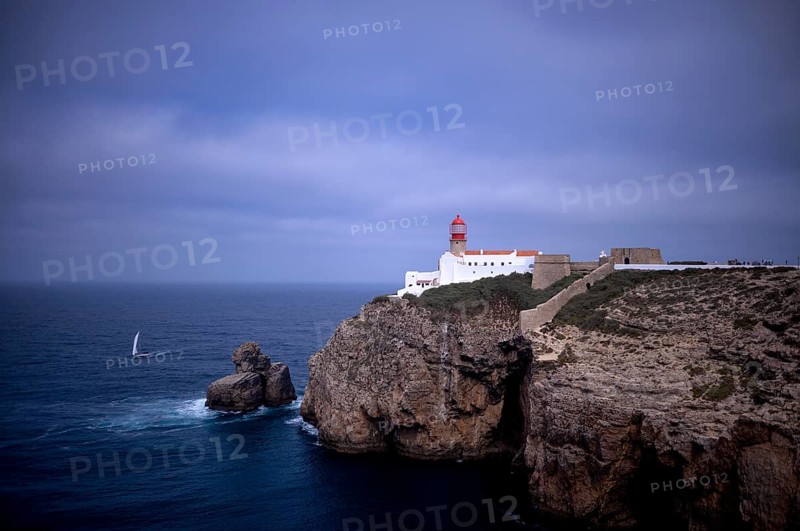 Sailing boat in front of the lighthouse Farol do Cabo de São Vicente, Cape St. Vincent, Sagres, steep coast, Atlantic Ocean, Algarve, Portugal, Europe