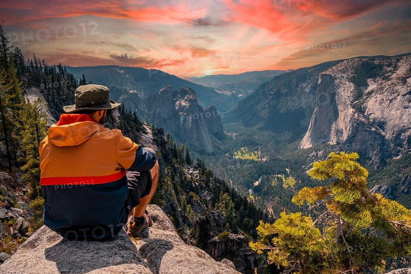 A young man on the trek sitting on the Sentinel Dome lookout in Yosemite National Park looking at El Capitan Mountain. United States
