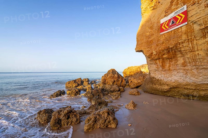ROCKFALL UNSTABLE CLIFFS, KEEP A SAFE DISTANCE is written in English on a warning sign in Portugal on the cliffs of the Atlantic Ocean. Rocks and stones break out here again and again and injure people., Albufeira, Faro, Portugal, Europe