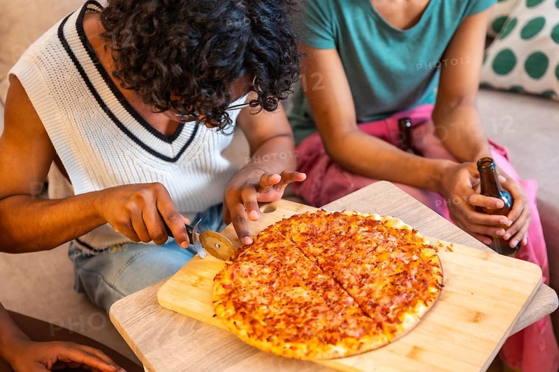 Close-up of man cutting homemade pizza to share with friends at home