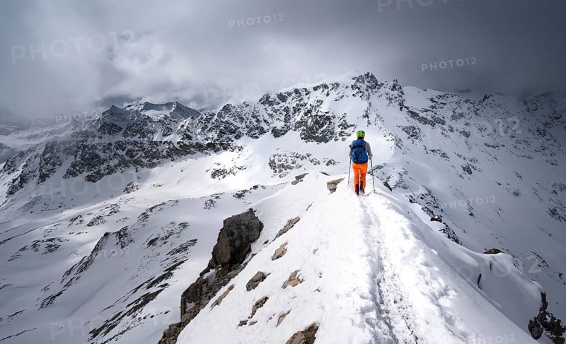 Mountaineer descending the narrow ridge of Piz Laviner, view of mountain panorama in wintry mountain landscape with dramatic clouds, Grisons Haute Route, Albula Alps, Rhaetian Alps, Grisons, Eastern Switzerland, Switzerland, Europe