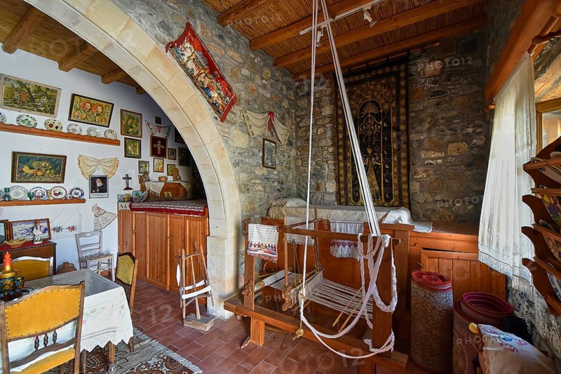 A traditionally furnished interior with stone walls, a wooden ceiling and a loom in the centre, surrounded by handicrafts and decorations, Folklore Museum, Asklipio village, Asklipion, Rhodes, Dodecanese, Greek Islands, Greece, Europe