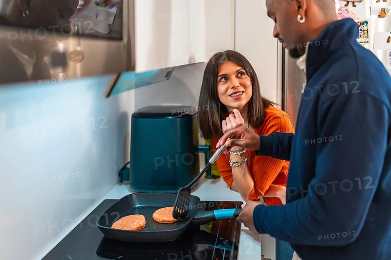 Happy multiethnic couple preparing burgers in a pan in their modern kitchen, enjoying their time together