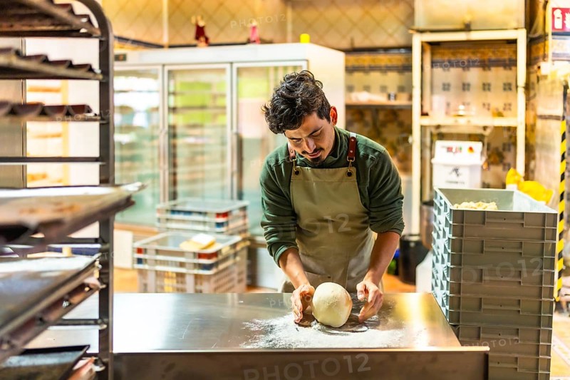 Latin young male baker kneading the raw dough in the kitchen of an artisan workshop