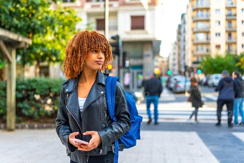 Latin young woman carrying bag in the city holding phone and looking at directions