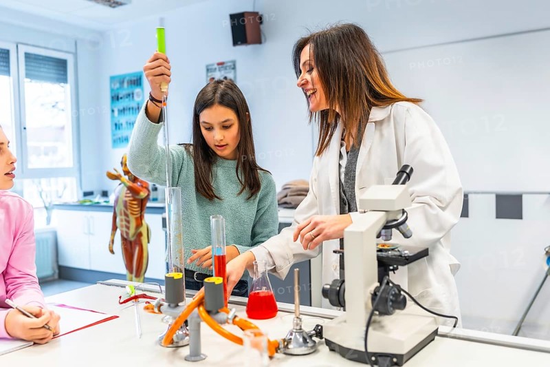 Female teacher assisting student using laboratory equipment during a chemistry experiment in a science classroom