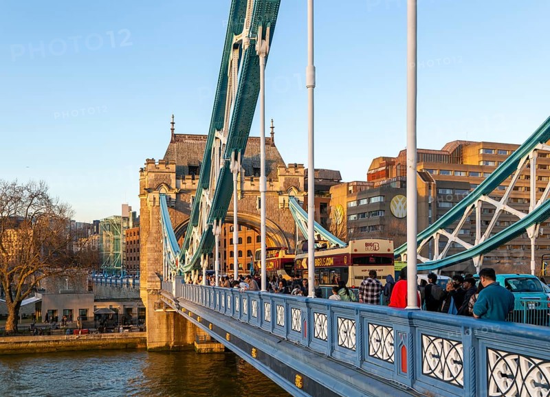People and open top tour buses cross Tower Bridge in late afternoon, London, England, UK