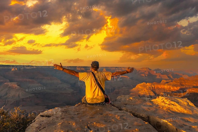 A young man sitting with his hands open and wearing a yellow shirt at Sunset at the Powell Point of Grand Canyon. Arizona, vertical photo