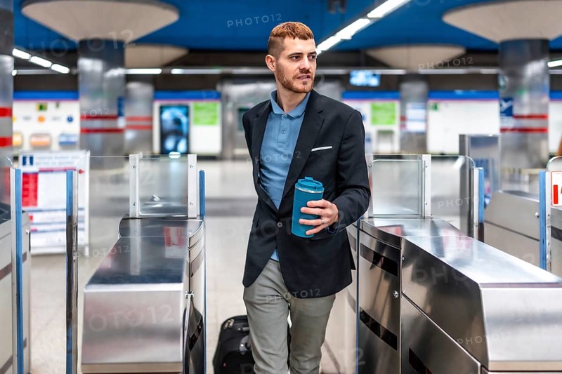 Young professional walking through subway turnstile holding reusable coffee cup, commuting to work in the morning