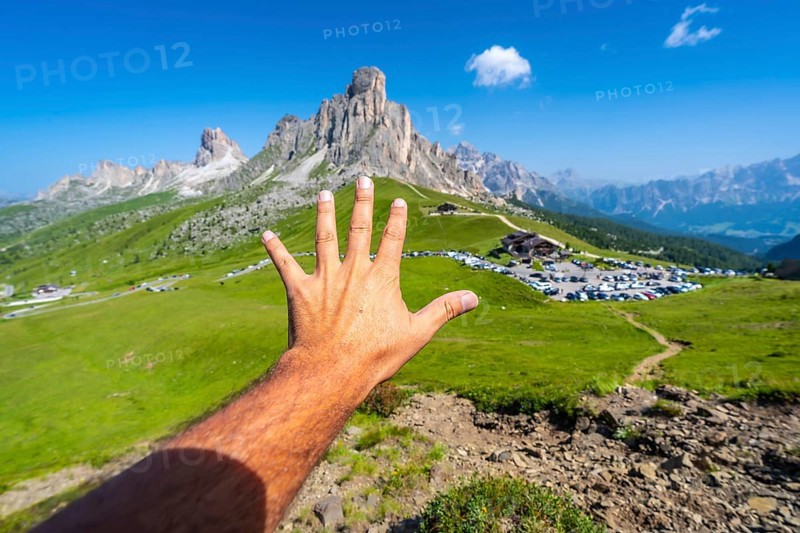 Male tourist showing five fingers with the majestic nuvolau peak and the passo giau mountain pass in the background on a sunny summer day