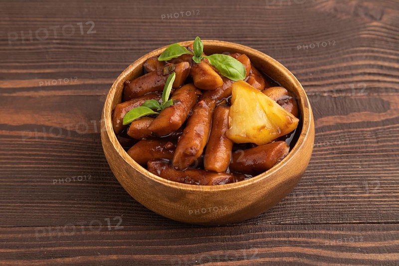 Tteokbokki or Topokki, fried rice cake stick, popular Korean street food with spicy jjajang sauce and pineapple on brown wooden background. Side view