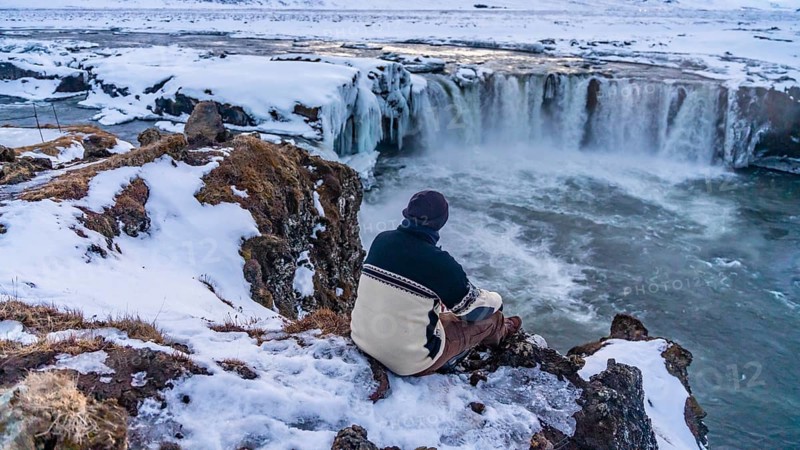 A man sitting looking at the frozen Godafoss waterfall at sunset in winter, Iceland, Europe