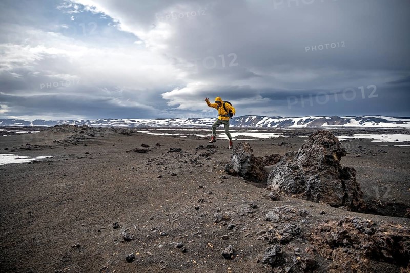 Hiker jumps into the air, snow-covered volcanic landscape with volcanic sand and petrified lava, crater of Askja volcano, Icelandic highlands, Iceland, Europe