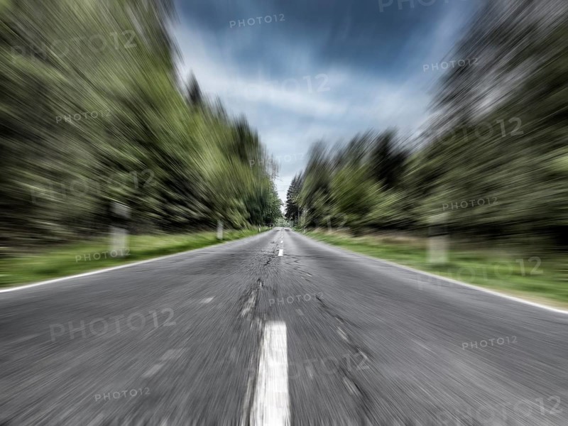 Photo with speed effect high speed speeding without speed limit from country road with central reservation leading to long straight ahead through mixed forest wooded area, Germany, Europe