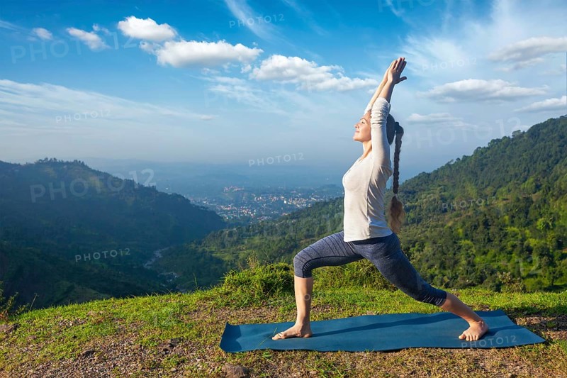 Yoga outdoors, sporty fit woman doing yoga asana Virabhadrasana 1, Warrior pose posture outdoors in Himalayas mountains in the morning