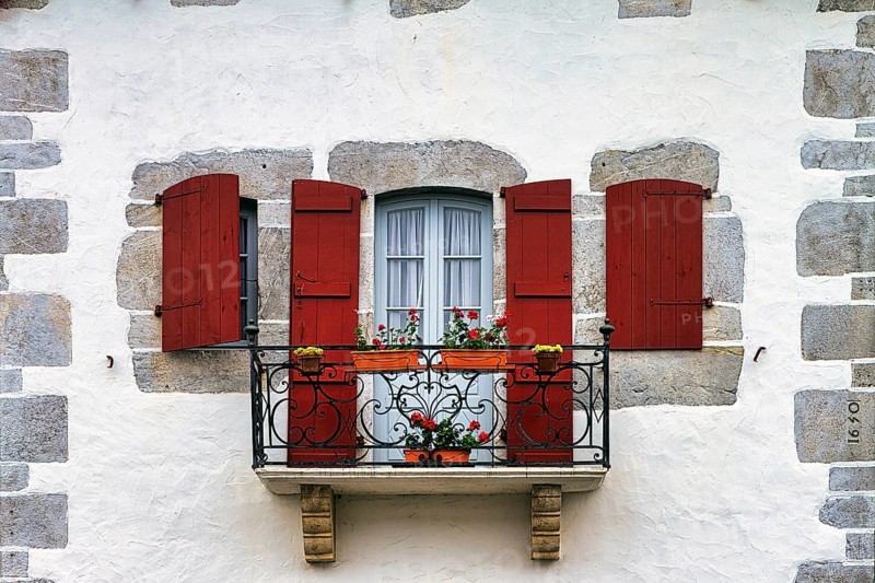 Typical window with balcony, red shutters and potted plants, detail of the façade, Espelette, Département Pyrénées-Atlantiques. Region Nouvelle-Aquitaine, Pays Basque, Basque Country, France, Europe