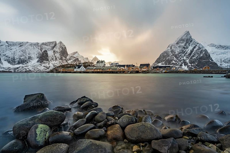 Traditional yellow rorbuer cabins on Sakrisøy Island, snow-capped rocky mountains in the back, Sakrisoy, Reine, Lofoten, Norway, Europe