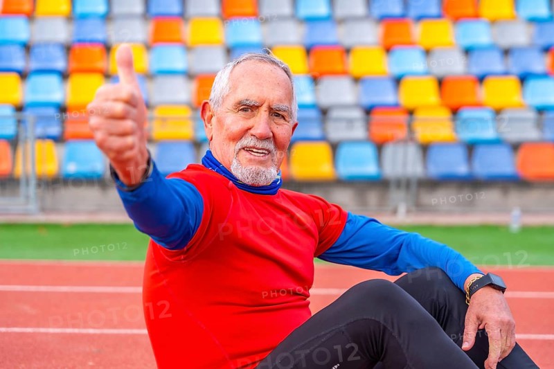 Proud senior man gesturing with thumbs up sitting on a running track after running