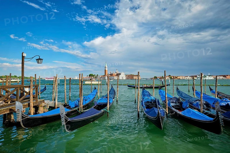 VENICE, ITALY, JUNE 27, 2018: Gondolas and gondolier in lagoon of Venice by Saint Mark (San Marco) square with San Giorgio di Maggiore church in background in Venice, Italy, Europe