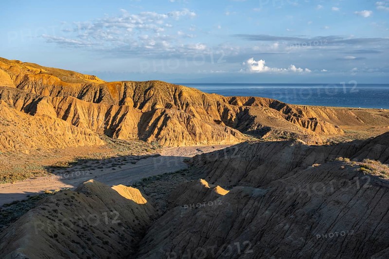 Canyon runs through a landscape of eroded hills at sunrise, Badlands, Issyk Kul Lake in the background, Canyon of the Forgotten Rivers, Issyk Kul, Kyrgyzstan, Asia