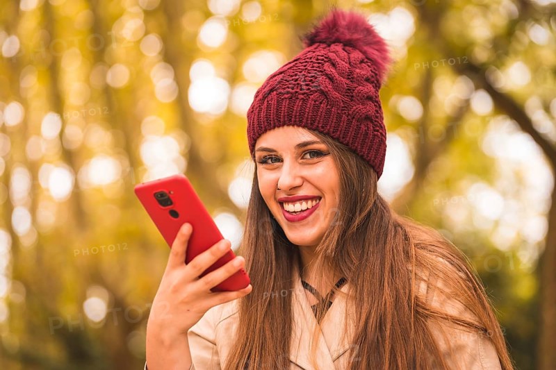 Portrait of a beautiful woman in autumn next to a forest in nature smiling sending a voice note with the phone