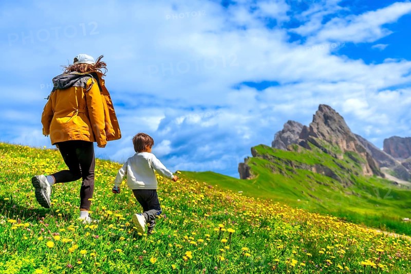Tourists running on a flowery meadow with the odle and seceda mountains in the background, dolomites, italy