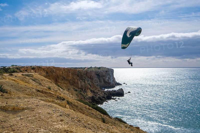 Sagres, Algarve, Portugal - Paraglider flying on the town beach Praia da Mareta, at the back left the viewpoint Ponta da Atalaia