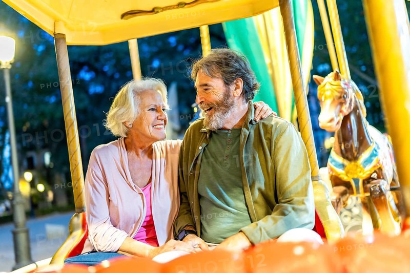 Happy senior friends sitting together in an old fashion carousel illuminated by light at night in the city