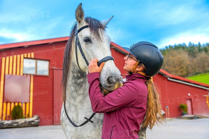 Female young jockey with helmet caressing a horse head on a equestrian center