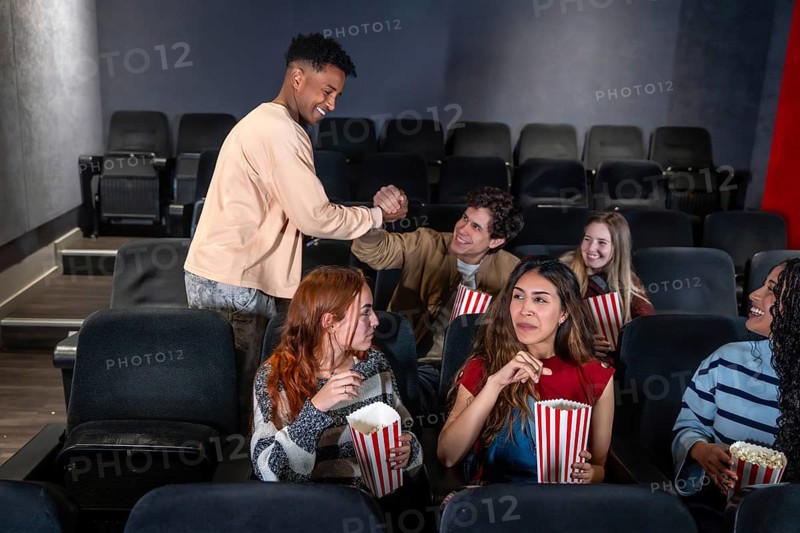 Young people enjoying a movie night out at the cinema, greeting each other and eating popcorn