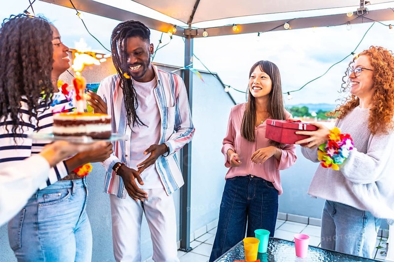 African happy woman receiving a gift and birthday cake celebrating with multi-ethnic friends in a terrace