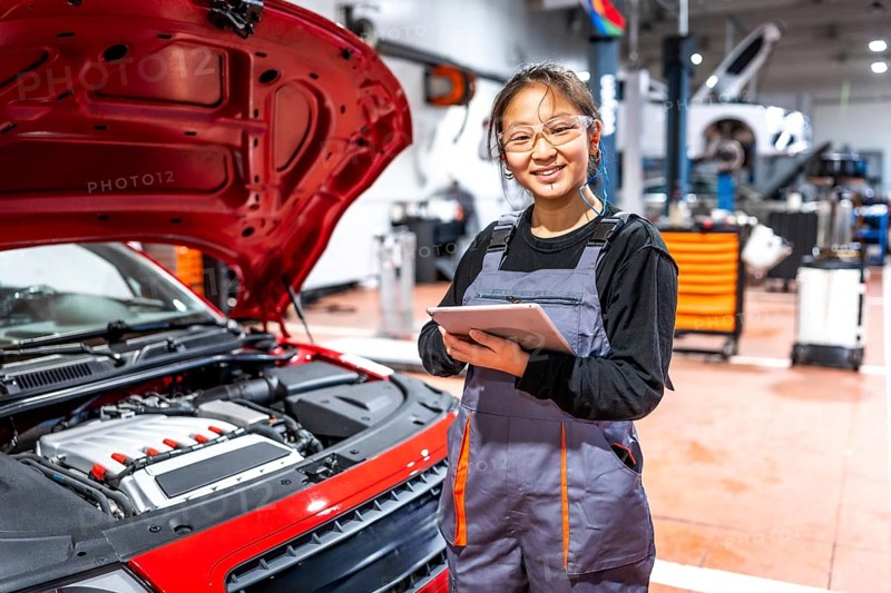 Confident female mechanic using a digital tablet, inspecting a car engine in a professional auto repair shop